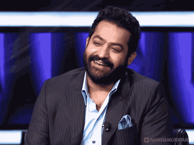 a man with a beard wearing a suit and a blue shirt with nandamurifan written on the bottom right