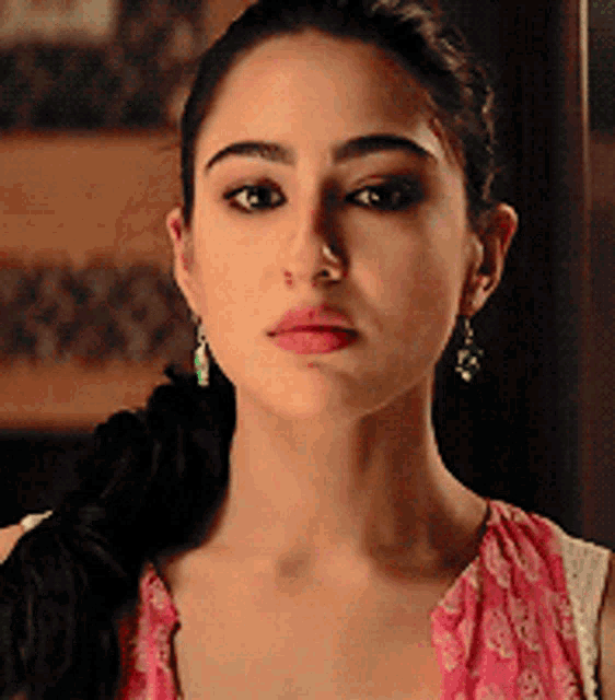 a close up of a woman 's face wearing earrings and a pink top