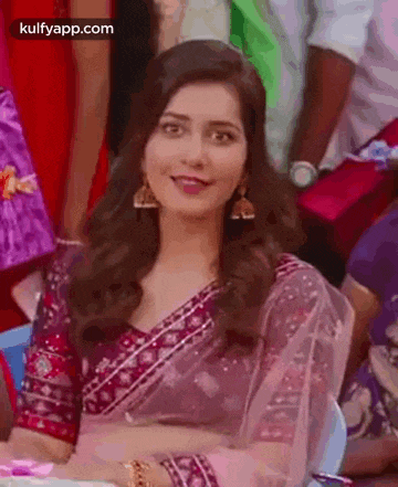 a woman in a purple saree is sitting at a table with a group of people .