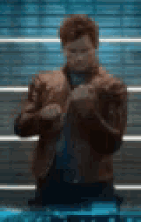 a man in a brown leather jacket is standing in front of a brick wall .