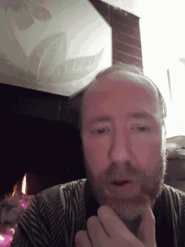 a man with a beard is standing in front of a fireplace looking at the camera