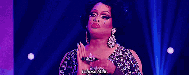 a drag queen is holding a sign that says milk and i chose milk