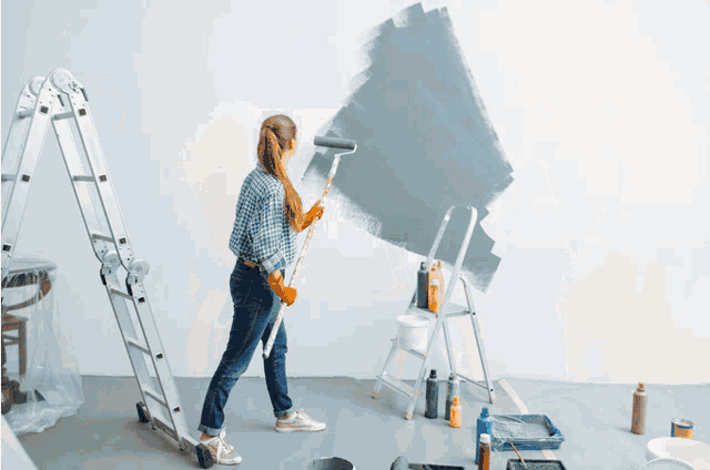 a woman paints a wall with a roller and a ladder in the background