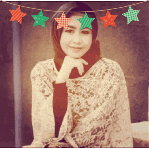 a woman wearing a hijab is smiling in front of a christmas bunting