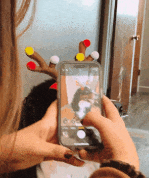 a person taking a picture with a cell phone with a reindeer antlers on their fingers
