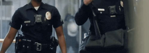 two police officers are walking down a hallway and one has a badge that has the letter e on it