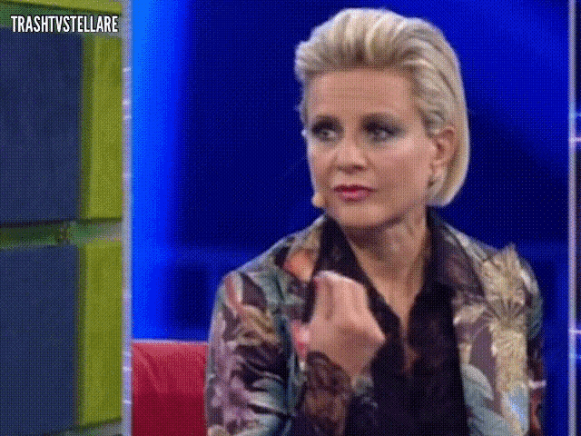 a woman in a floral jacket is sitting in front of a blue wall with the words trashtvstellare above her