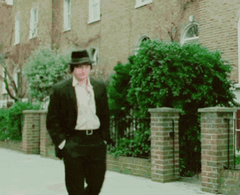 a man in a suit and hat walking down a street