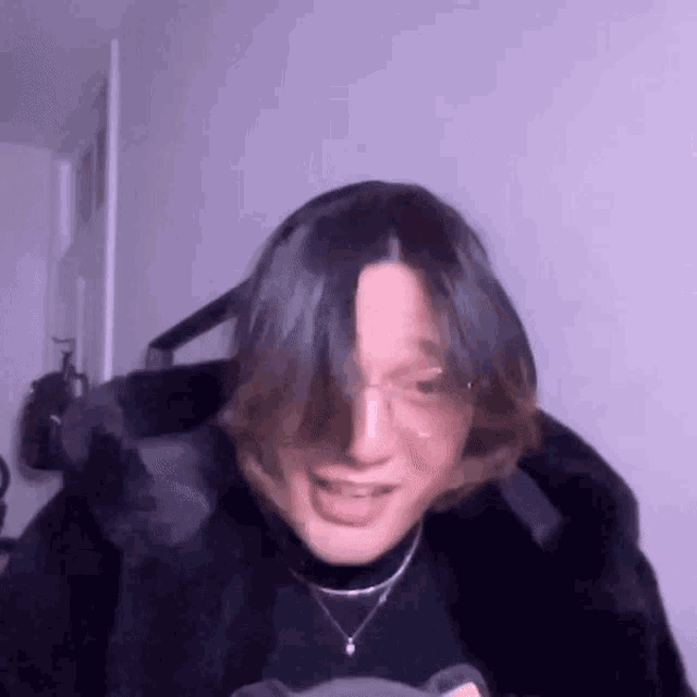 a person with long hair and glasses is wearing a black fur coat and a black turtleneck .