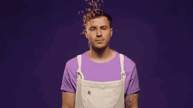 a man wearing a purple shirt and white apron is covered in wood chips