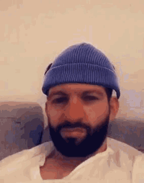 a man with a beard wearing a blue beanie and a white shirt .
