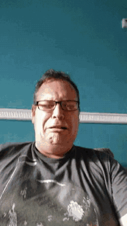 a man wearing glasses and a black shirt is sitting in front of a blue wall