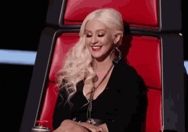 a woman with blonde hair is sitting in a red chair smiling