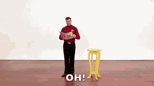 a man in a red shirt and black pants is standing next to a yellow table with the words oh written on it .