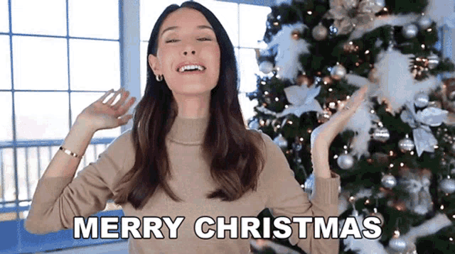 a woman is standing in front of a christmas tree and says merry christmas