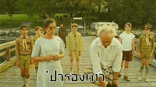 a group of people are standing on a wooden bridge with the words " ปา รอ ง เท รา " in the bottom right