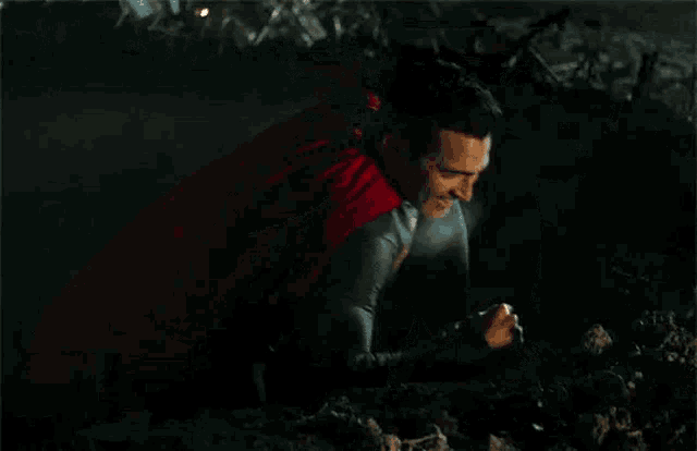 a man in a superman costume is laying on the ground with a torch in his hand .