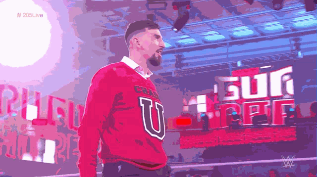a man in a red sweater stands in front of a screen that says # 205live