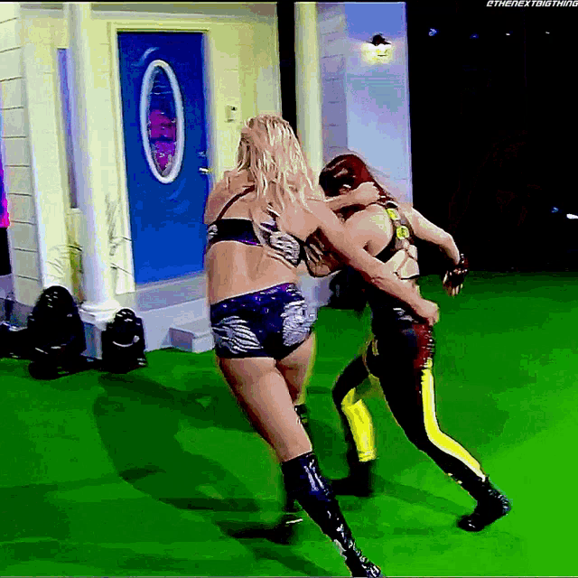 two women are wrestling in front of a blue door that says ' the next thing ' on it