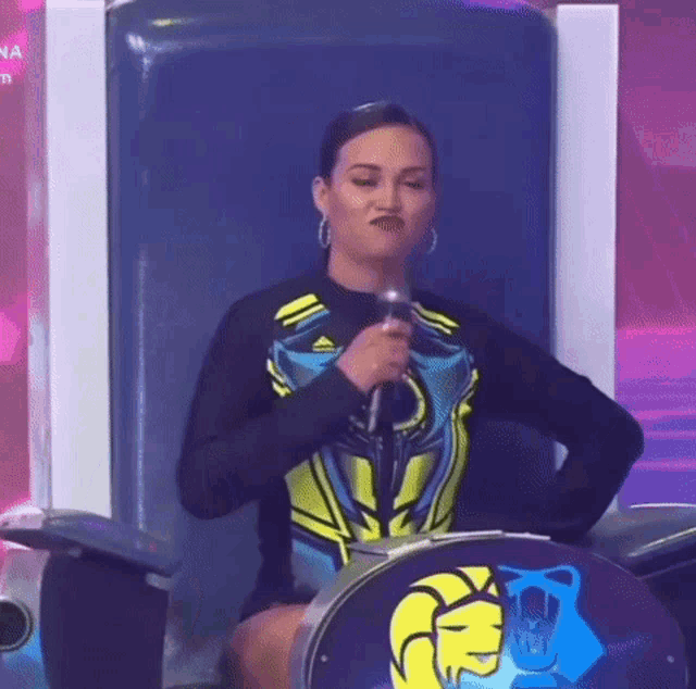 a woman is sitting in a chair with a microphone in her hand and making a funny face .