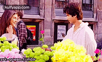 a man and a woman are standing next to each other in front of a flower stand .