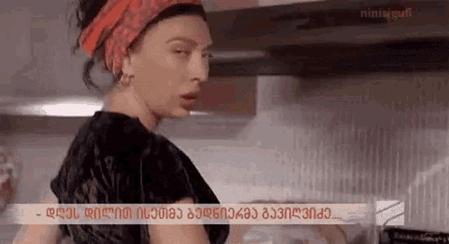 a woman is standing in a kitchen wearing a red headband and earrings .