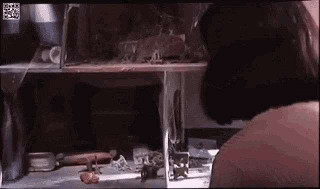a woman is sitting at a table in front of a shelf with a broken glass .