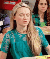 a girl in a blue top is sitting at a table with her eyes closed .