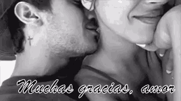 a black and white photo of a man kissing a woman on the neck .