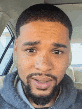 a man with a beard is sitting in a car and making a funny face