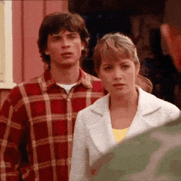 a man in a plaid shirt and a woman in a white jacket are standing next to each other in front of a building .
