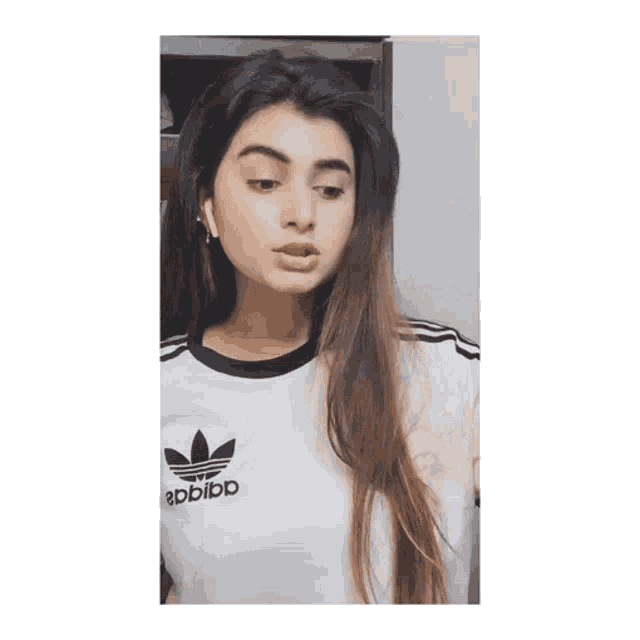 a woman wearing a white adidas shirt looks at the camera