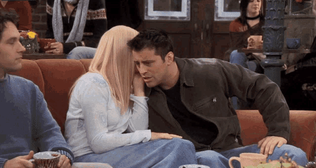 a man and a woman are sitting on a couch and the man has the word no on his jacket