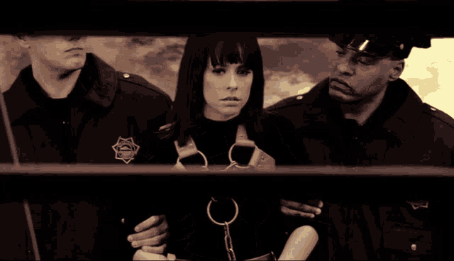 a woman in handcuffs is being escorted by two police officers with a sheriff 's badge on their jackets