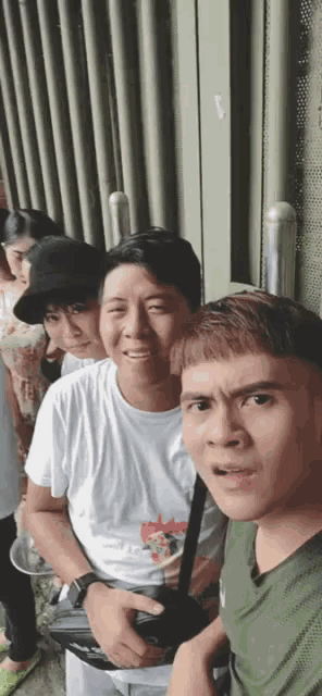 a group of people are standing next to each other in front of a building and taking a selfie .
