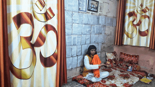 a man sits on a blanket in front of a wall with a painting of an om symbol