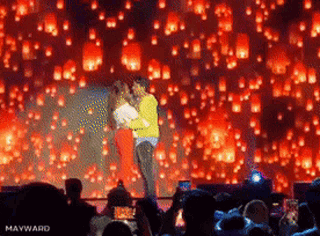 a man and woman are kissing on a stage with lanterns floating in the air