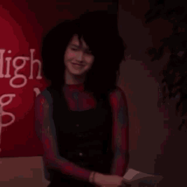 a woman is smiling in front of a red sign while holding a piece of paper .