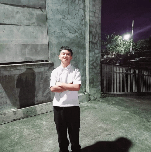 a young man with his arms crossed stands in front of a wall