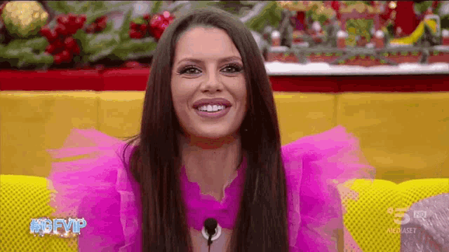 a woman in a pink dress is smiling while sitting on a couch .