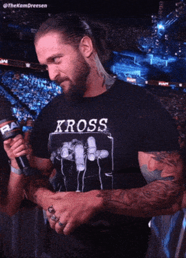 a man wearing a black shirt that says kross is talking into a microphone