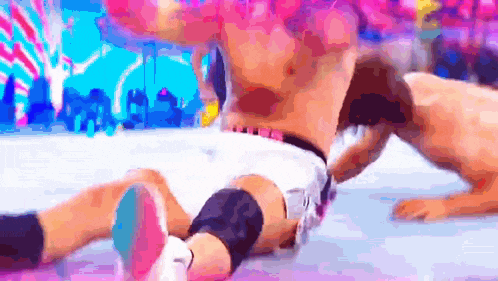 a man is laying on the ground in a wrestling match with a pink background