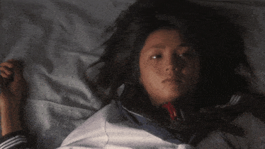 a girl in a school uniform is laying on a bed with headphones around her neck