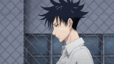 a man with black hair and a white shirt stands in front of a chain link fence