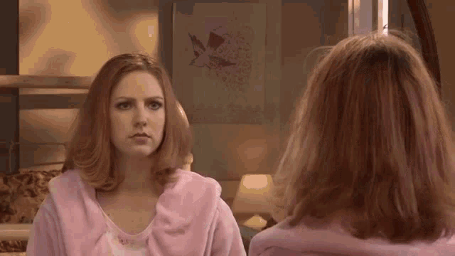 a woman in a pink robe is looking at her reflection in a mirror .