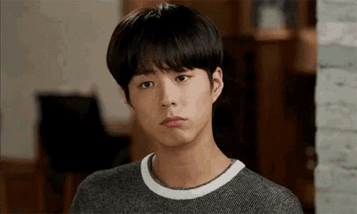 a young man is making a funny face while wearing a gray sweater .
