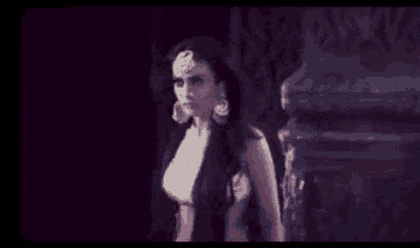 a woman with long hair and earrings is standing in a dark room in a black and white photo .