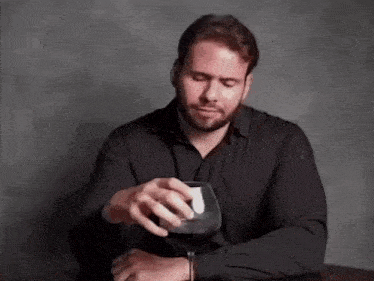 a man is sitting at a table holding a glass of wine .