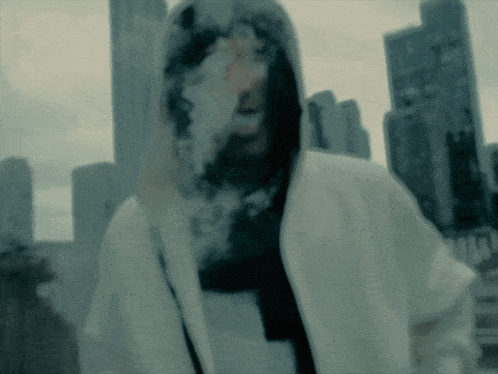 a man in a white hoodie smoking a cigarette in front of a city skyline