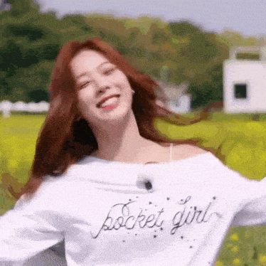 a woman is standing in a field with her arms outstretched and wearing a white shirt that says pocket girl .